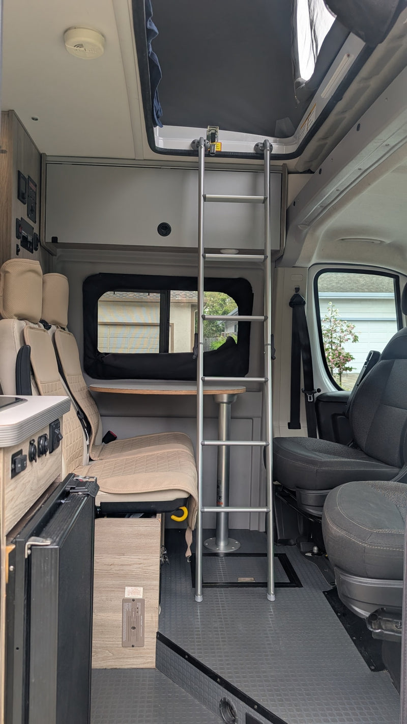  showing front swivel seats and a rear dining area with two beige seats.|RV rental camper van interior showing a compact kitchen with a sink — photo 12