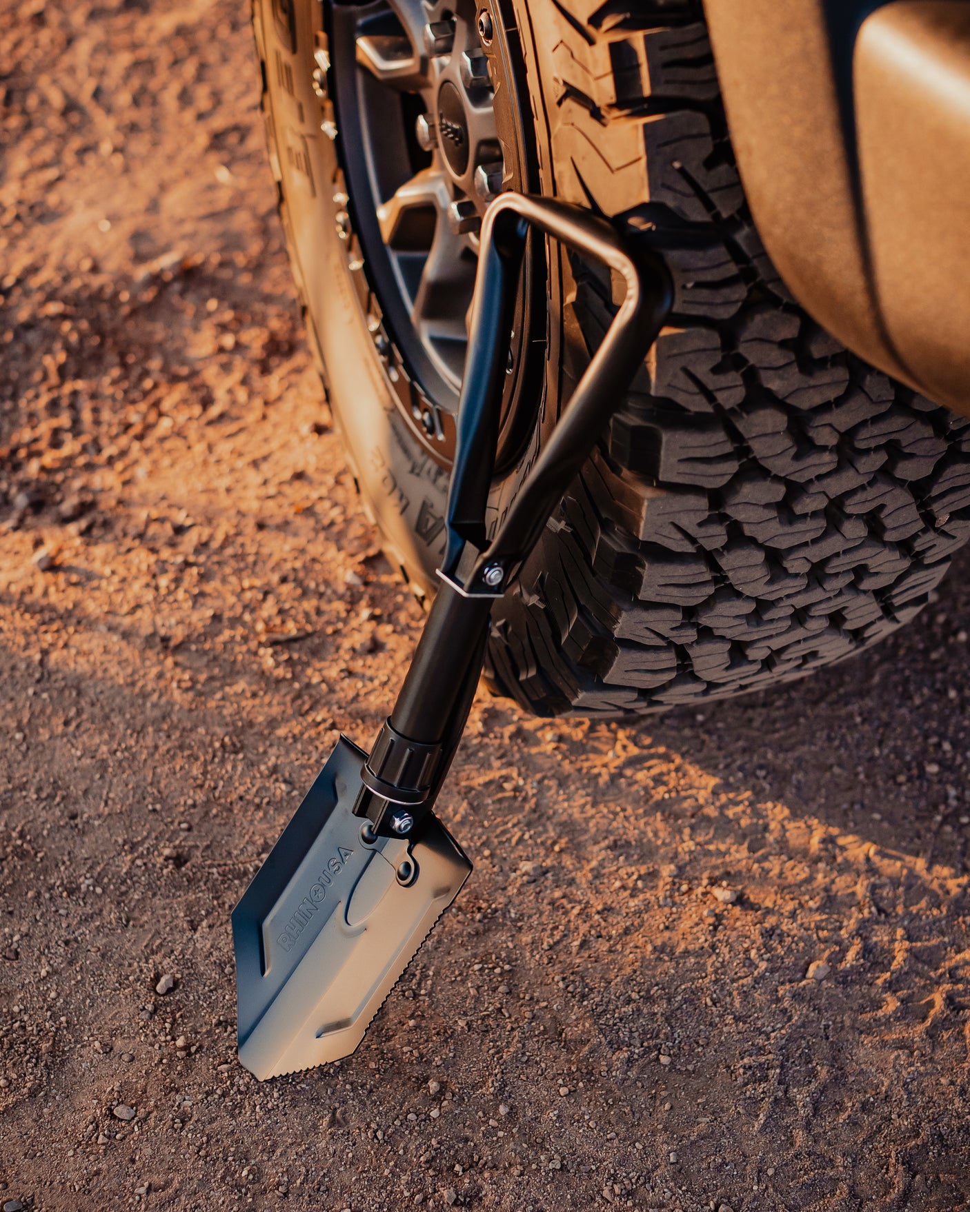 Essential gear for your RV rental adventure: a RHINO USA tactical shovel leans against an RV tire on a dirt road.