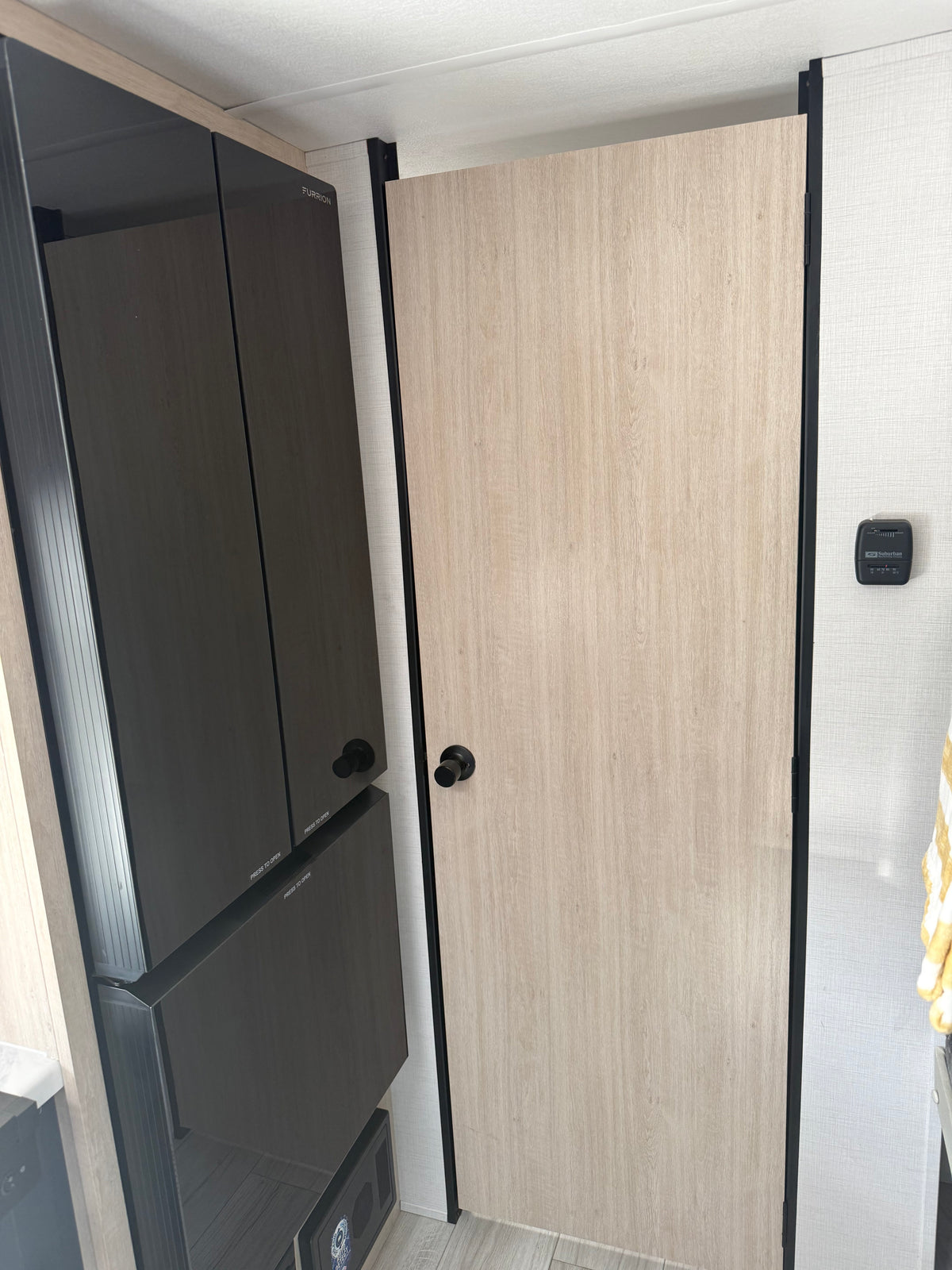RV rental interior with a light wood door, a dark Furrion refrigerator unit, and a Suburban thermostat on the textured wall. — photo 5