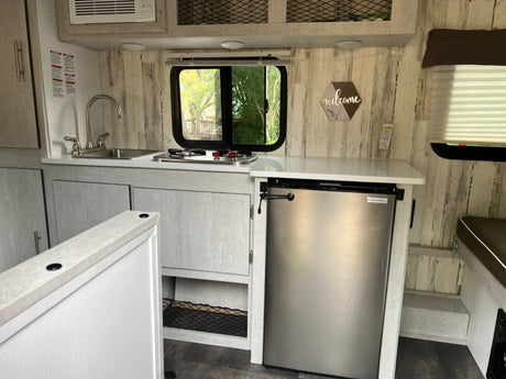 This rv rental features a compact kitchen with a sink, two-burner stove, refrigerator, and bright wood-panel walls.