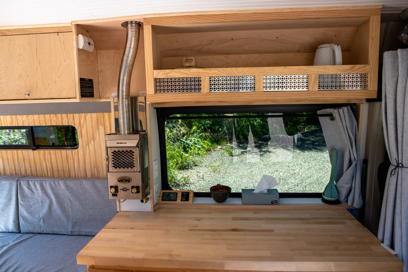 Cozy RV rental interior with wooden built-ins, Dickinson heater, and large window. Perfect for van life adventures.