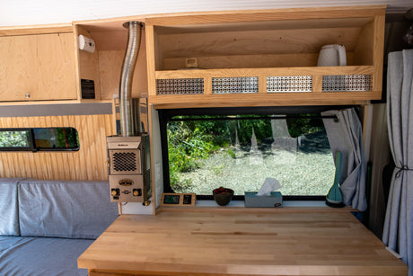 Cozy RV rental interior with wooden built-ins, Dickinson heater, and large window. Perfect for van life adventures.