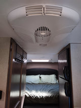 View into an RV rental bedroom from the living area, showing a bed, ceiling AC unit, and side-mounted refrigerator.