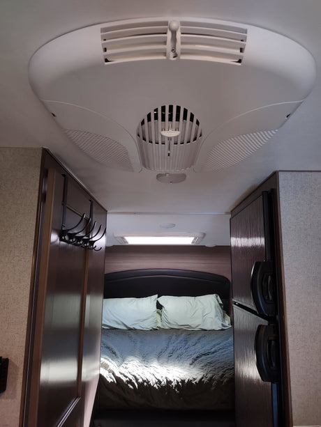 View into an RV rental bedroom from the living area, showing a bed, ceiling AC unit, and side-mounted refrigerator.