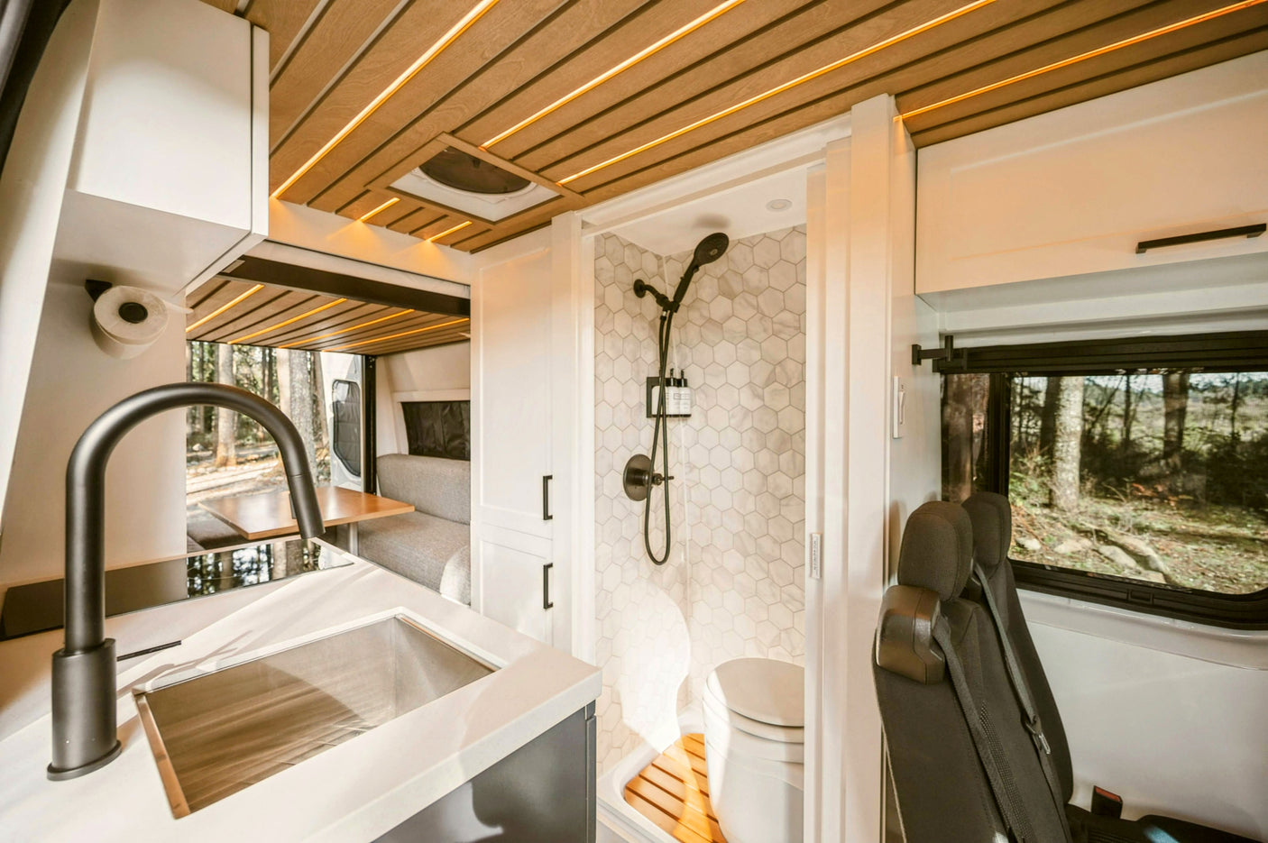 Spacious RV rental interior with a modern kitchen, hexagonal-tiled shower, toilet, and comfortable dinette, surrounded by nature.