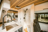Spacious RV rental interior with a modern kitchen, hexagonal-tiled shower, toilet, and comfortable dinette, surrounded by nature.