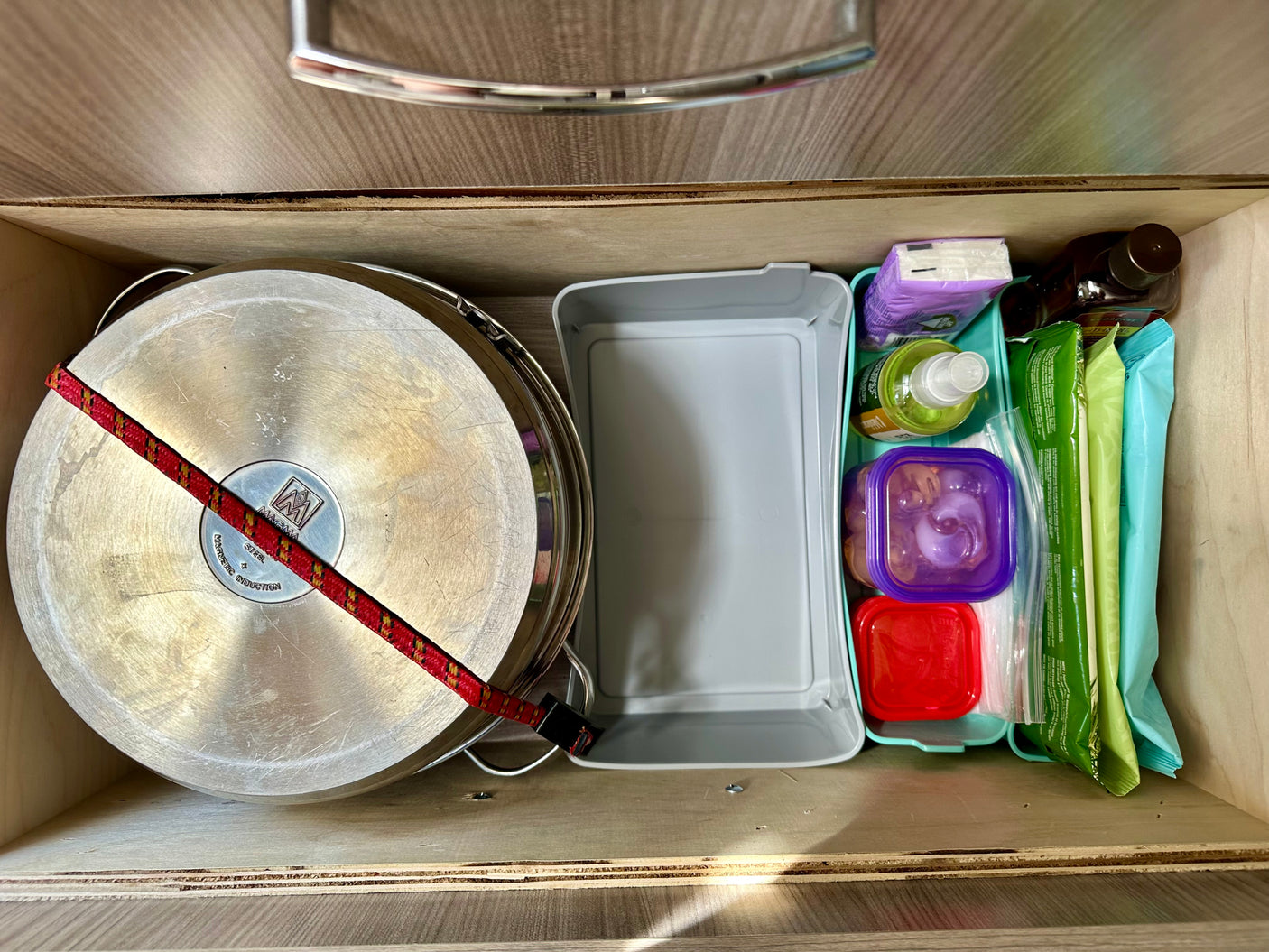 Inside an RV rental drawer: pots secured with a bungee, plus organized household supplies and food containers.