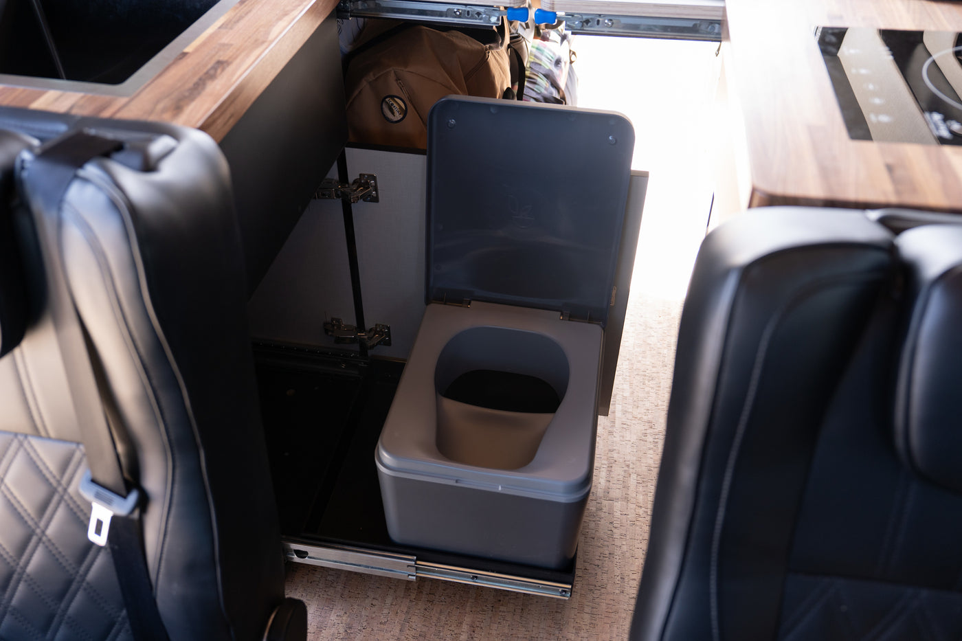 RV rental: Pull-out portable toilet nestled between passenger seats, alongside a compact kitchen counter and storage. — photo 7