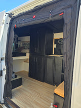 Inside this RV rental: light wood flooring, black cabinets, a sink, comfy bed, and door privacy curtains.