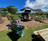 Adventure awaits with this Jeep RV rental & rooftop tent at a scenic Hawaiian campsite, featuring outdoor cooking gear.