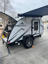 A sleek grey FREESOLO teardrop camper RV rental with an open rear galley kitchen and extended awning. Ready for adventure.