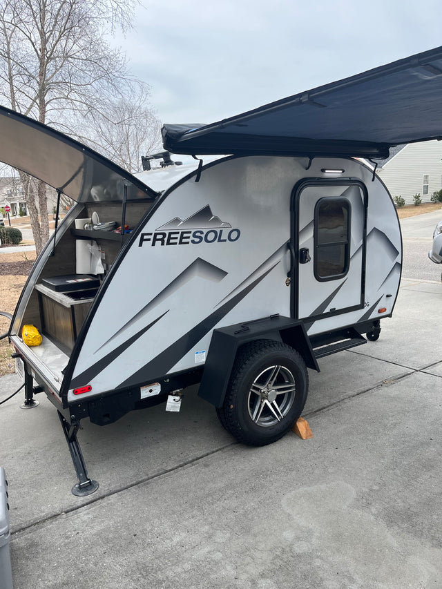 A sleek grey FREESOLO teardrop camper RV rental with an open rear galley kitchen and extended awning. Ready for adventure.