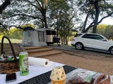 Peaceful RV rental camping setup: Airstream Basecamp, white SUV, and a picnic table with Shiner beer.