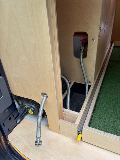 Custom RV rental water system: Flexible hoses connect to a tank with a red valve in this van conversion's interior plumbing.