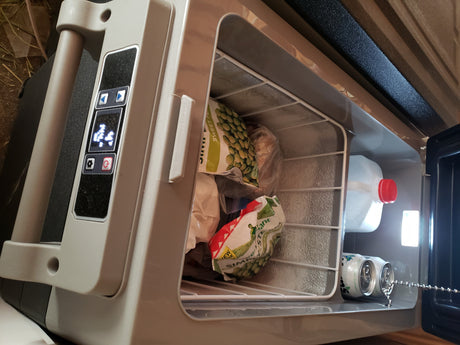 Open portable fridge/freezer, perfect for an RV rental, stocked with sweet peas, frozen food, drinks & water for cool travel storage.