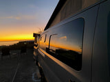 An rv rental camper van reflects a vibrant sunset over the ocean. Chairs await a peaceful evening view.