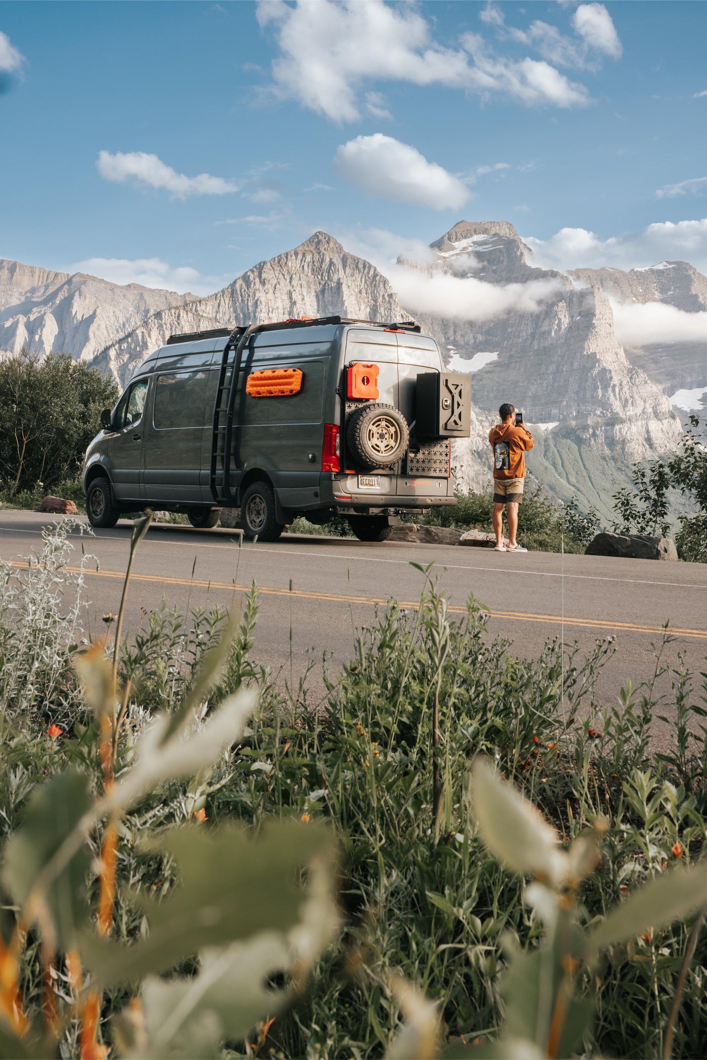 Gray camper van parked roadside amidst majestic mountains. A person captures the scenic views. Ideal for your RV rental getaway!