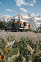 Gray camper van parked roadside amidst majestic mountains. A person captures the scenic views. Ideal for your RV rental getaway!