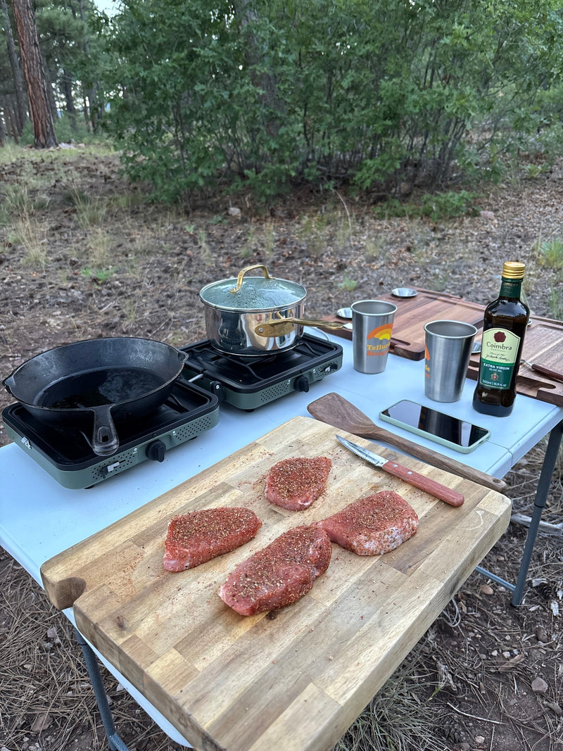 Outdoor cooking during an RV rental trip: seasoned meat, portable stove, skillet, and olive oil, set up in a forest. — photo 11