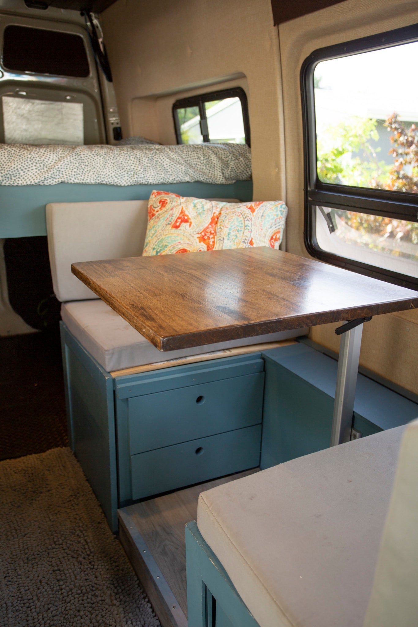 RV rental interior: dining area with wooden table, cushioned benches, storage drawers. Rear bed visible for compact living. — photo 3