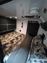 RV rental interior features patterned bedding, overhead storage, a fire extinguisher, and a smoke alarm for safety.