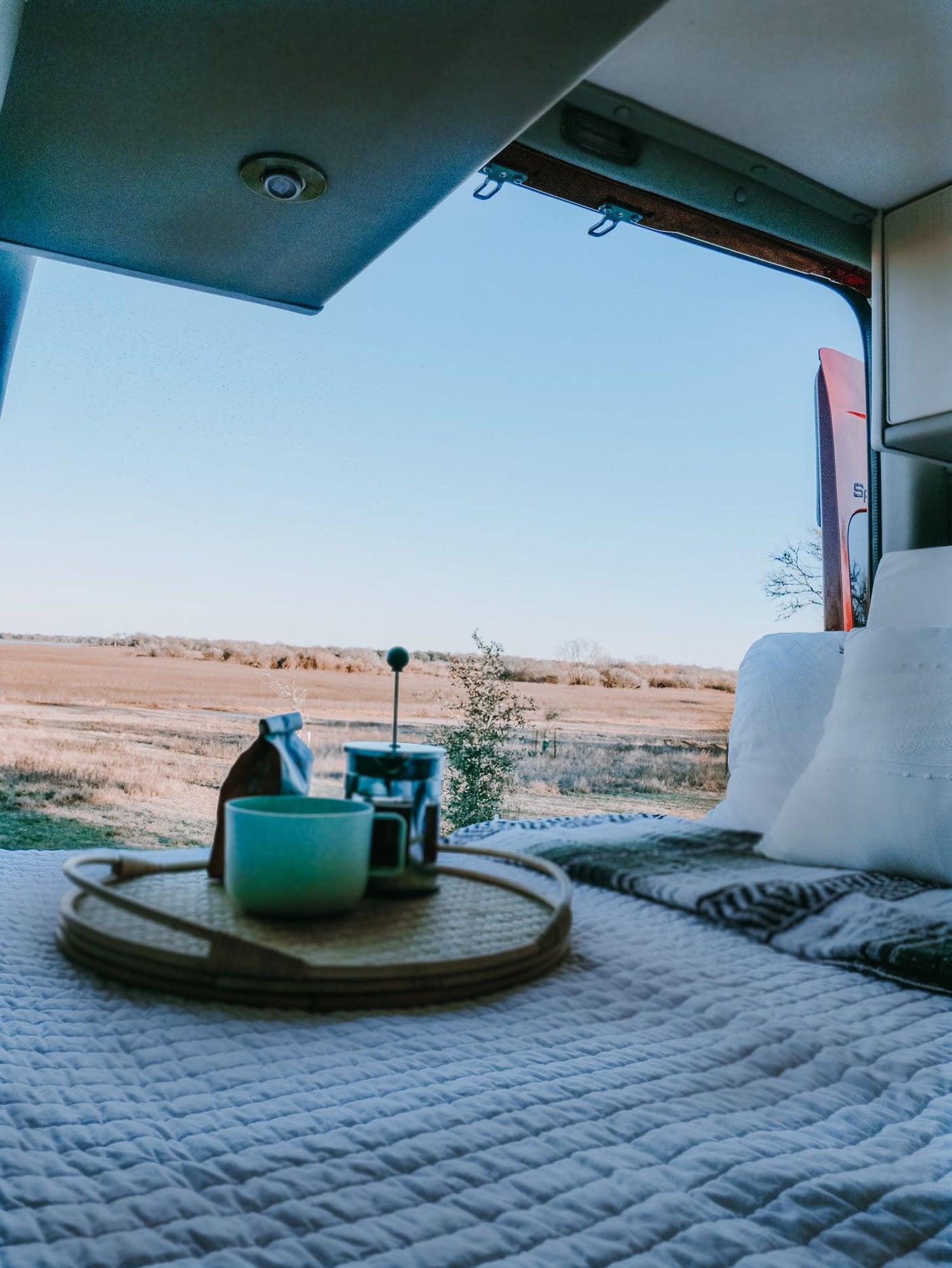 Experience the ultimate RV rental morning: cozy bed, coffee, and expansive nature views. Perfect van life escape.