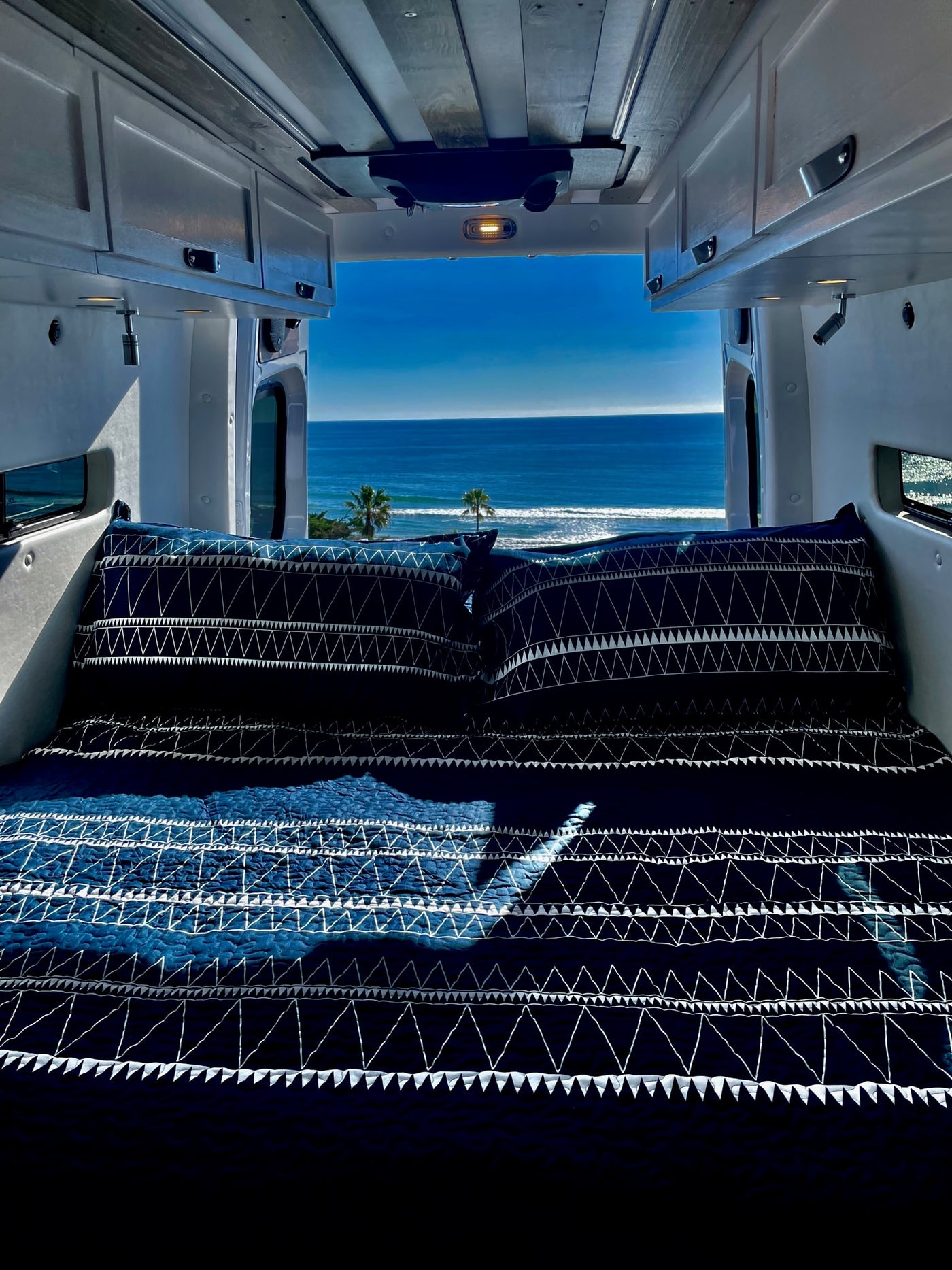 Inside an **rv rental**, a comfy bed offers stunning ocean views and distant palm trees. Ideal for a serene camper van getaway. — photo 4