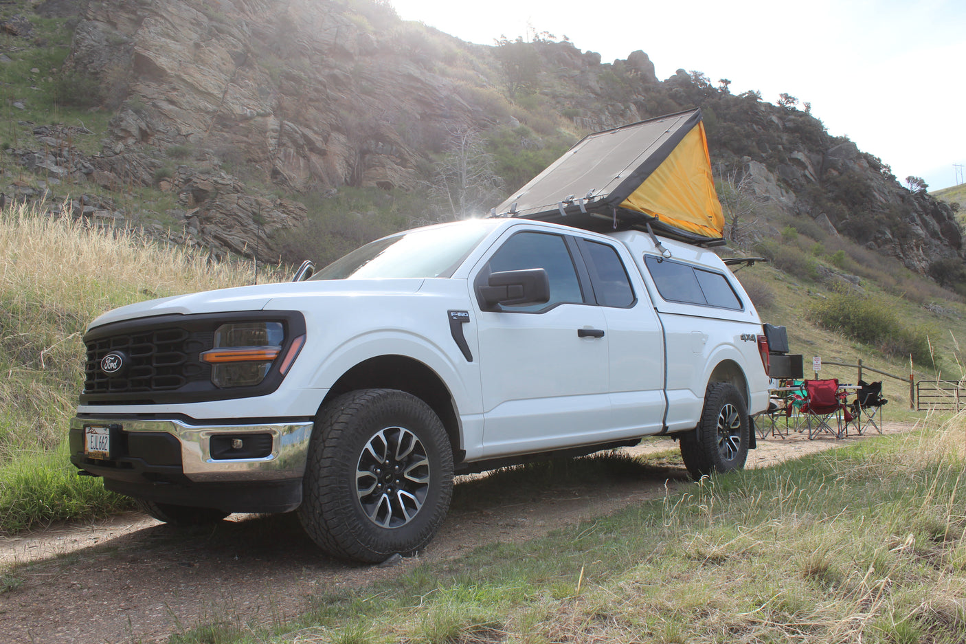 White Ford F-150 4x4 truck with a rooftop tent & camping setup. Perfect for an 'rv rental' adventure in rocky terrain.