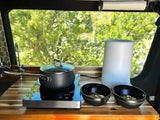Inside an RV rental, a compact kitchen with an induction cooktop, pot, bowls of food, and an air purifier.