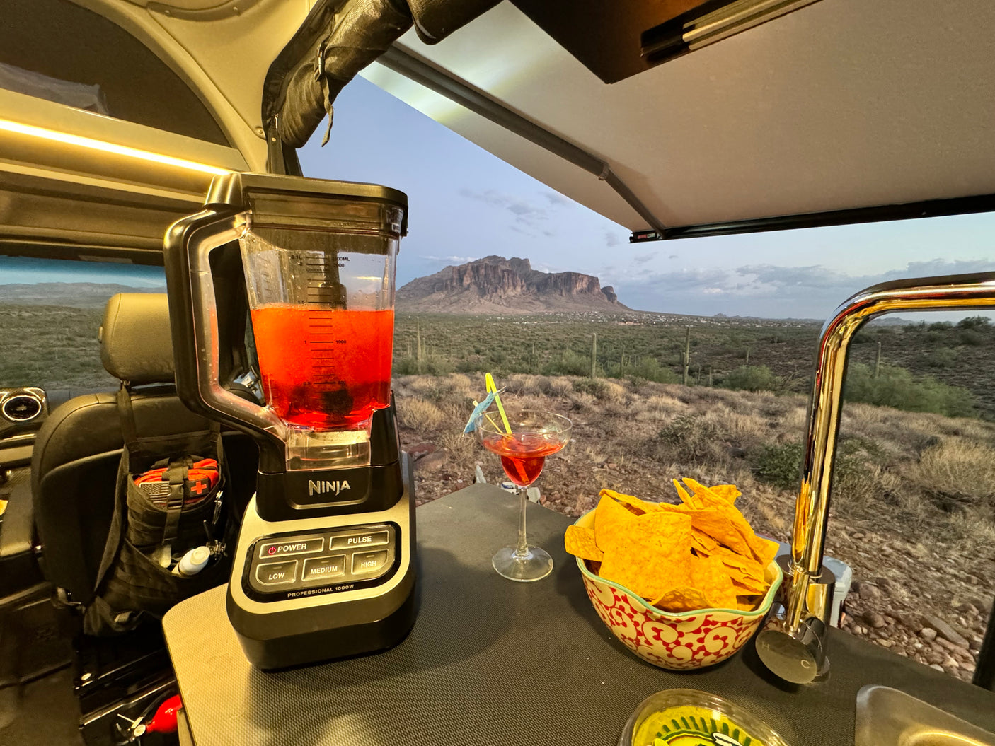 RV rental adventure: Enjoying cocktails & chips with a blender setup and stunning desert mountain views from inside a camper van.