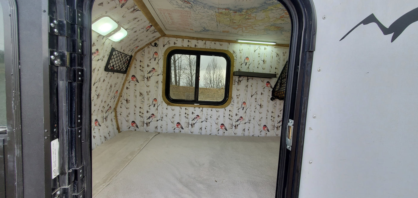 Explore this cozy RV rental interior: comfortable bed, unique bird & birch wall decor, map ceiling, and bright lighting.