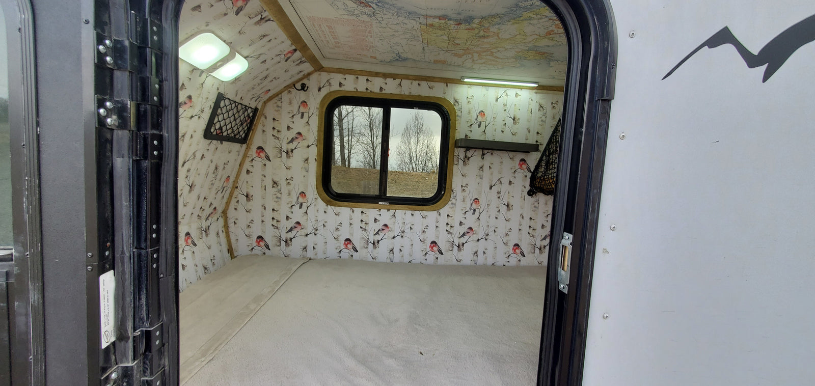 Explore this cozy RV rental interior: comfortable bed, unique bird & birch wall decor, map ceiling, and bright lighting.