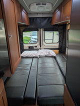 Cozy camper van interior with convertible bed/seating, perfect for an RV rental adventure. Features wood cabinets & AC.
