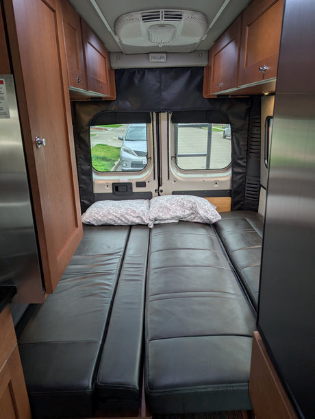 Cozy camper van interior with convertible bed/seating, perfect for an RV rental adventure. Features wood cabinets & AC.