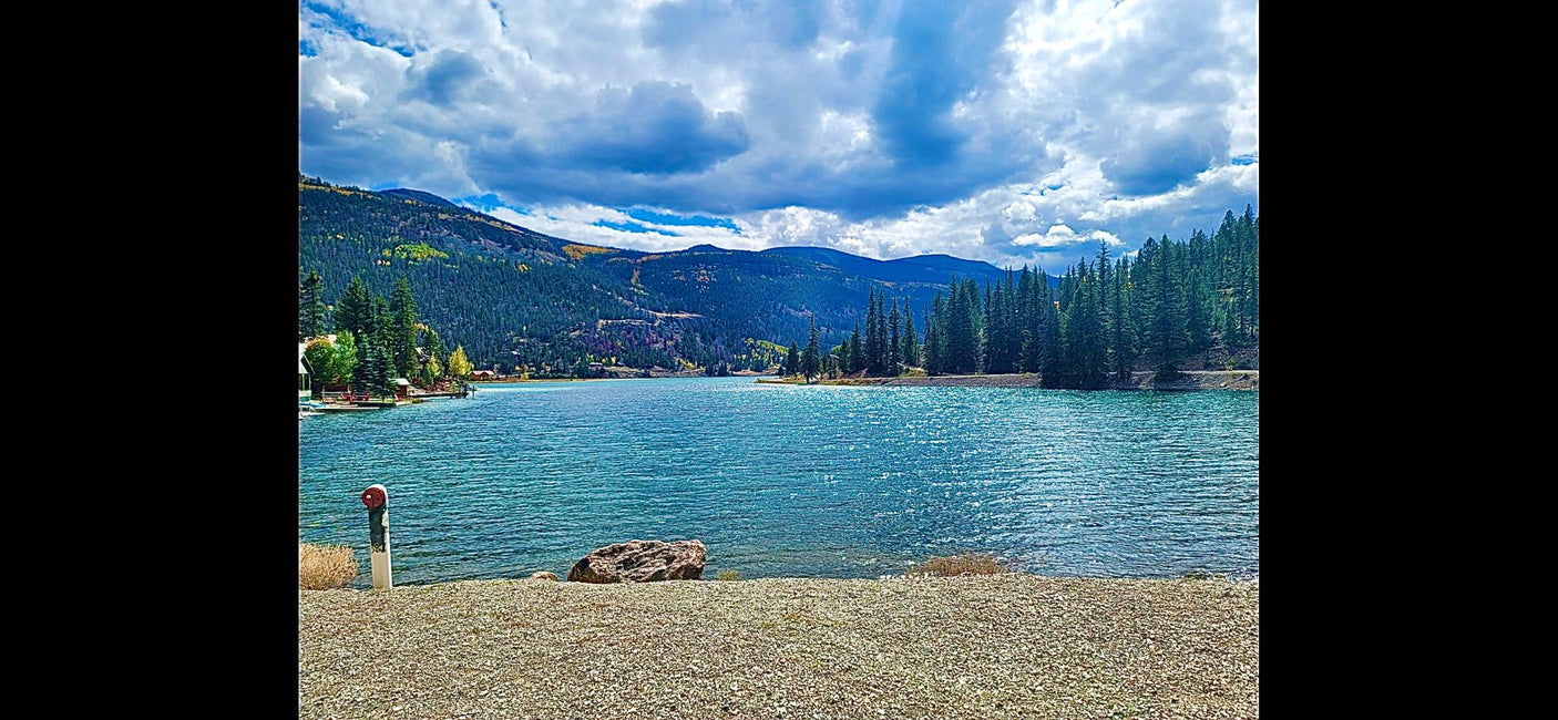 Beautiful blue mountain lake with pine forests, ideal for an RV rental getaway. Features a rocky shore & docks for recreation.