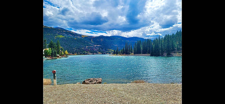 Beautiful blue mountain lake with pine forests, ideal for an RV rental getaway. Features a rocky shore & docks for recreation.