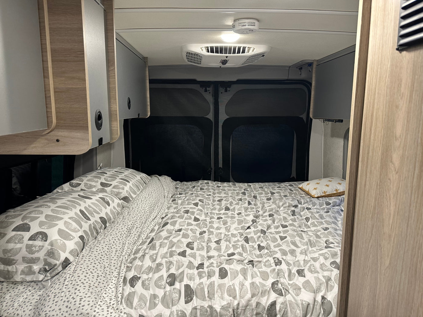 RV rental's cozy bedroom features patterned bedding, sleek overhead cabinets, and dark rear window screens for privacy. — photo 4