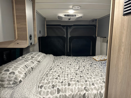 RV rental's cozy bedroom features patterned bedding, sleek overhead cabinets, and dark rear window screens for privacy.