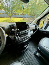 Interior view of an RV rental's cockpit, featuring a tablet on the dash, steering wheel, and a view of trees and a building.