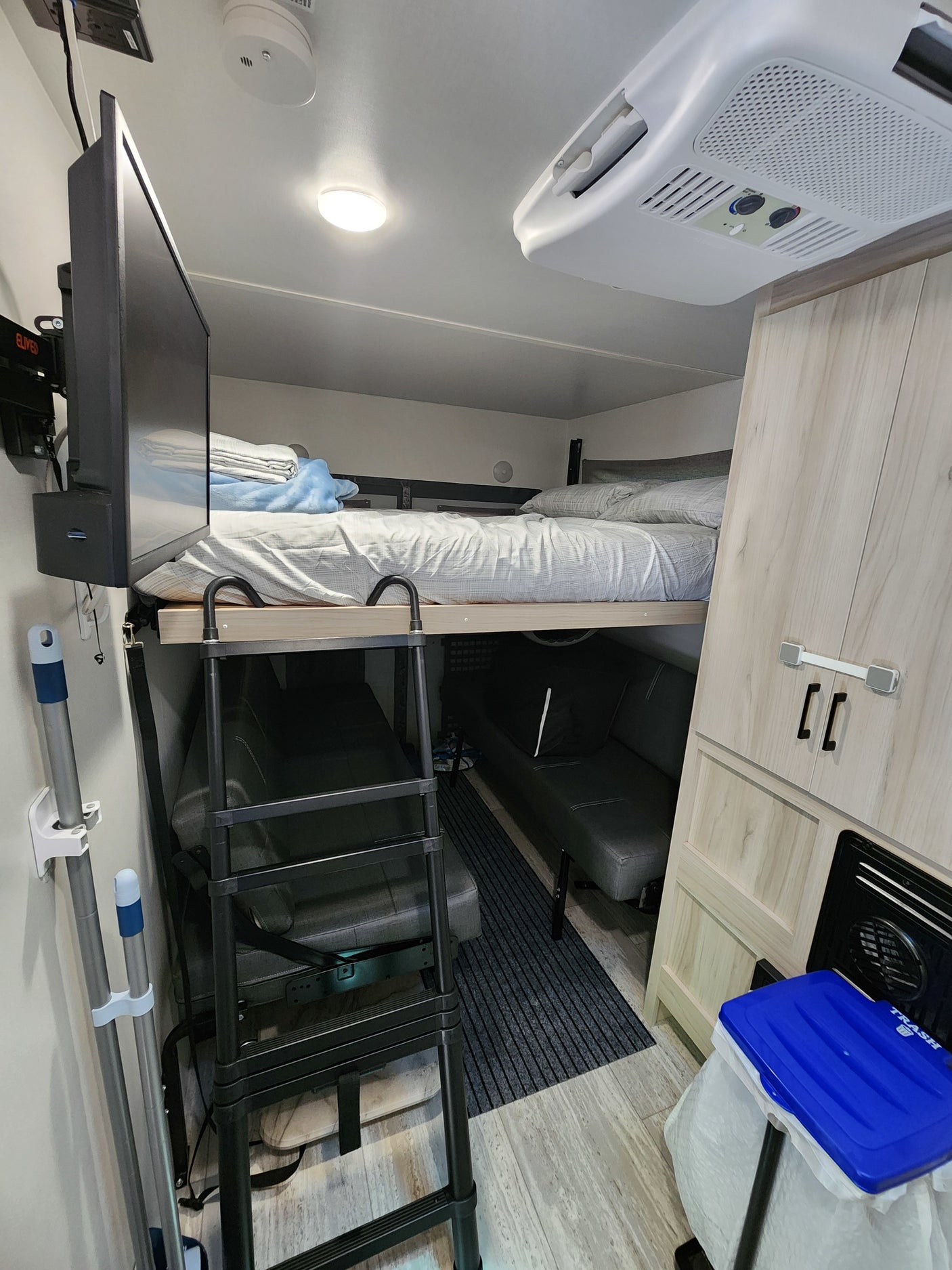 An RV rental's compact interior featuring bunk beds with a ladder, seating, and mounted TV.