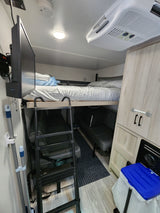 An RV rental's compact interior featuring bunk beds with a ladder, seating, and mounted TV.