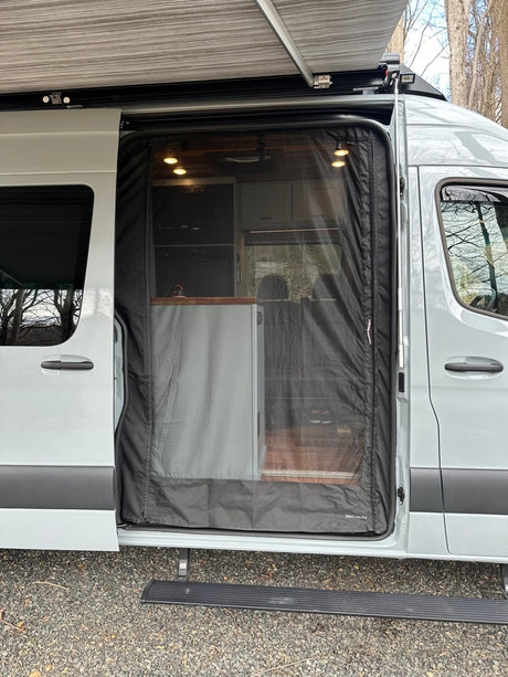 A light grey rv rental van, with its side door open, featuring a mesh screen and extended awning.