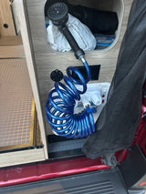 RV rental utility setup: a blue coiled outdoor shower hose with an adjustable head, ready for use. Perfect for camp life.