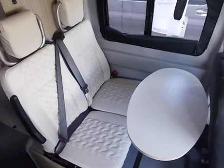 Bright, modern RV rental interior: white quilted seats and a round table for comfort on the road.