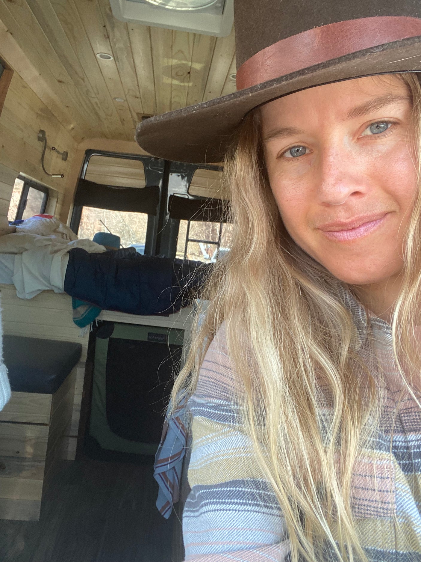 Smiling woman in her cozy RV rental, showcasing the custom wood-paneled interior. Ideal for mobile living.