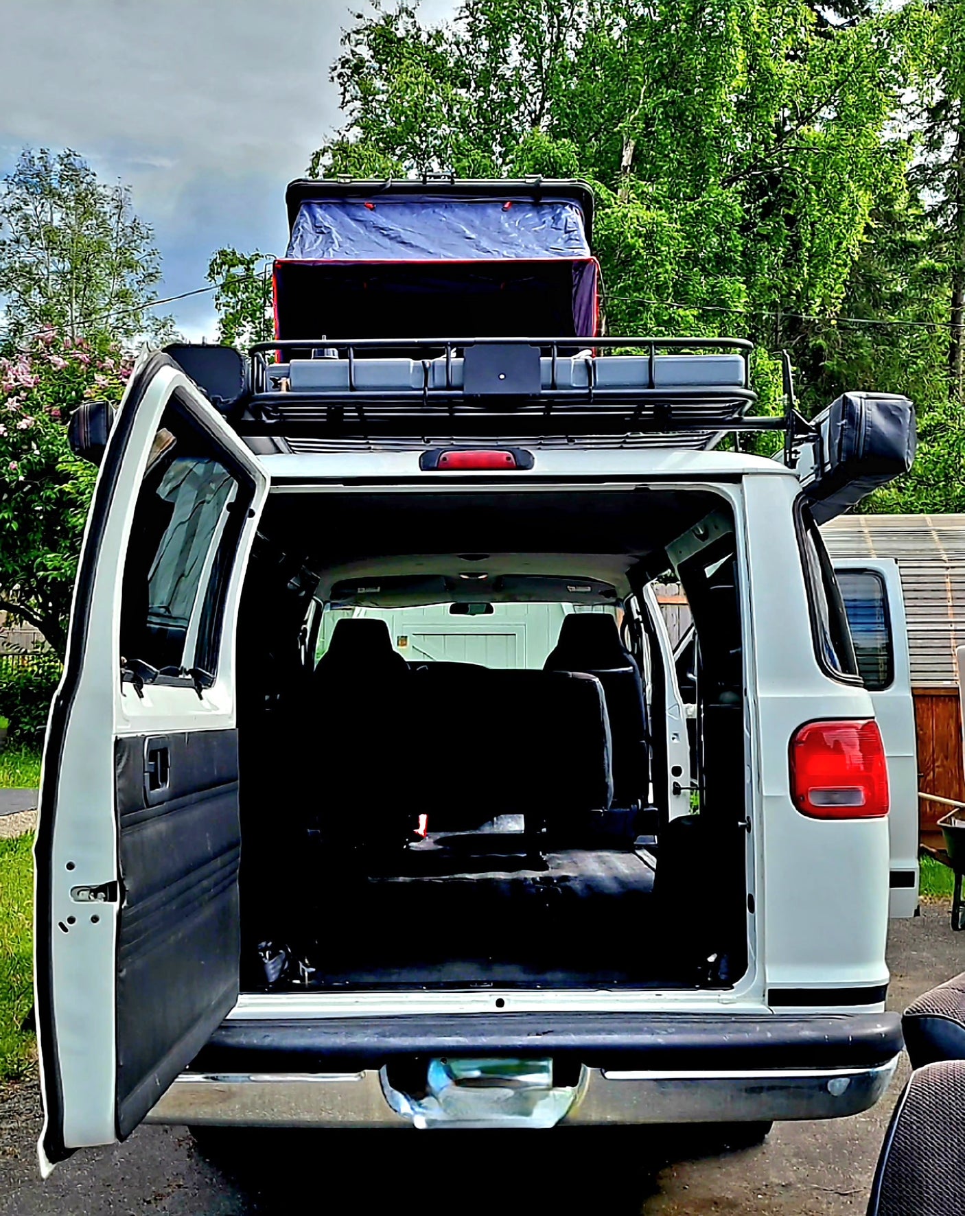 White **rv rental** van with rear doors open, revealing interior space, topped with a rooftop tent for camping adventures.