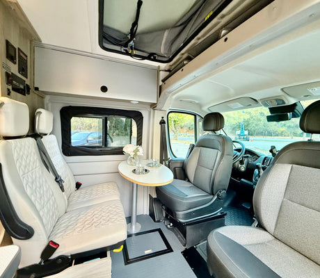 RV rental interior: swivel front seats, dining table, and plush white bench seating create a versatile living space.