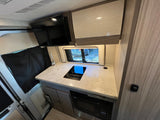 RV rental kitchen: counter, sink, induction cooktop, microwave, TV, and wood-grain cabinets.
