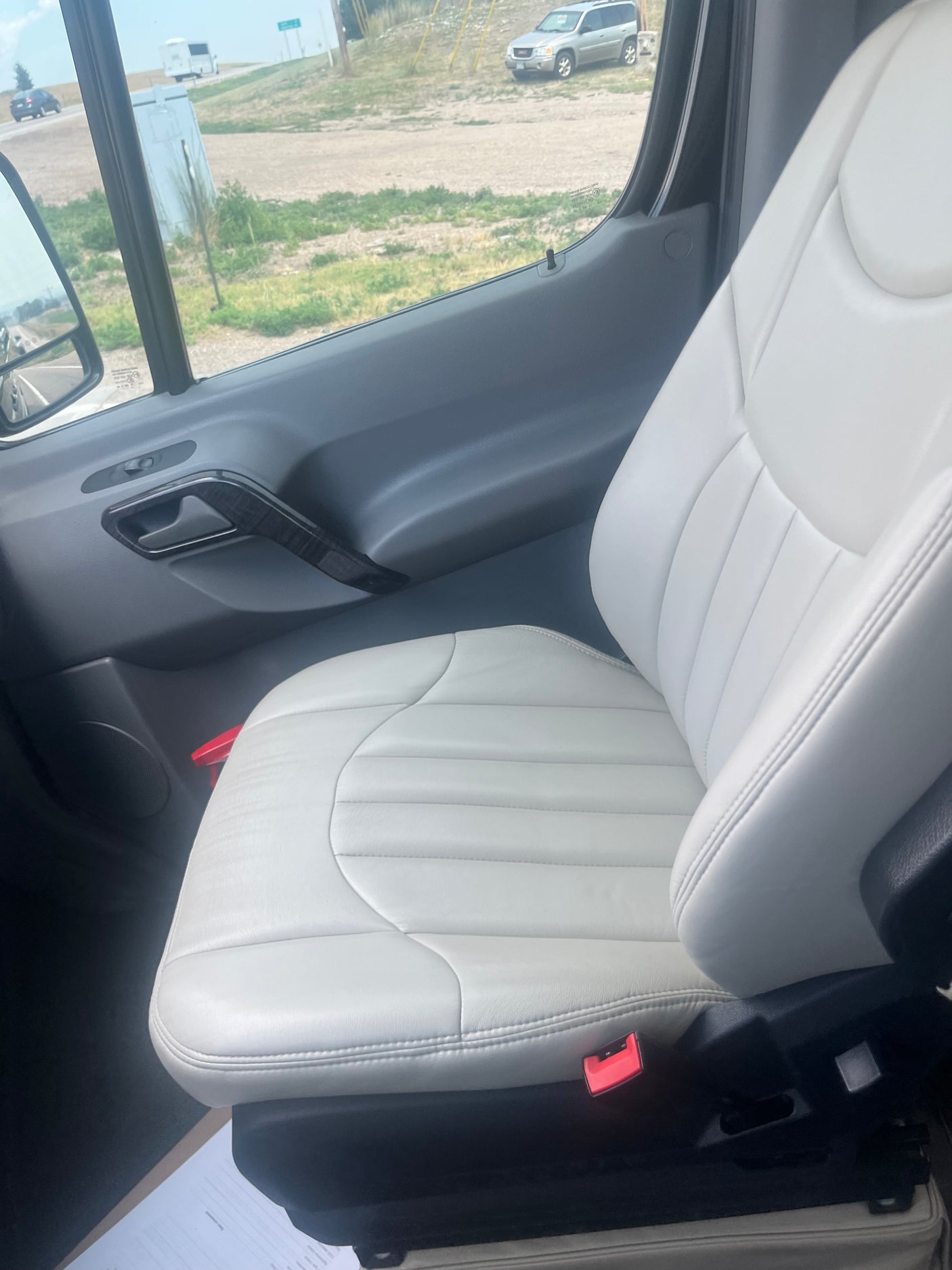 Inside an RV rental: a comfy light-colored passenger seat, looking out to a road with other vehicles.