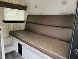Inside this cozy RV rental, find comfortable brown bench seating with a high back, pleated window shade, and light wood-look walls.
